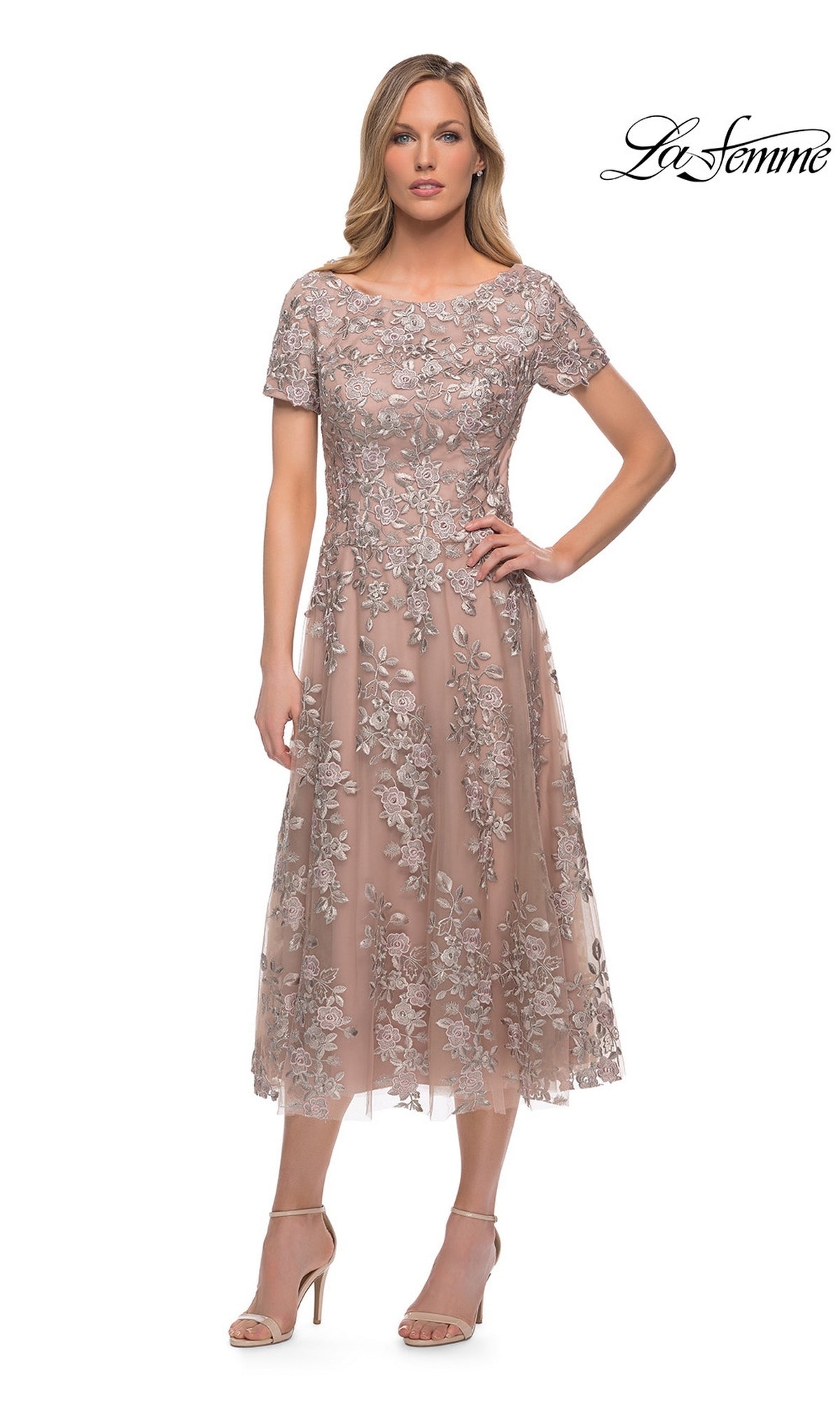 Woman in Midi Mother of Bride Dress: La Femme 29830, blush pink with floral lace embroidery and heeled sandals, posed against a white backdrop. “La Femme” logo top right.